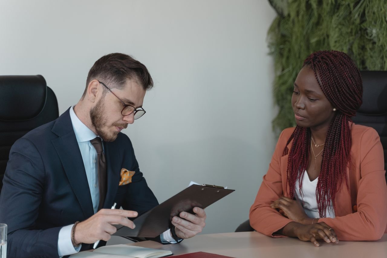 gallery-1 A man and woman engaging in a job interview in a modern office setting.